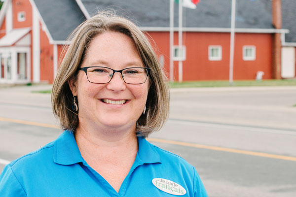 A woman in a blue shirt with short brown hair and glasses standing outside.