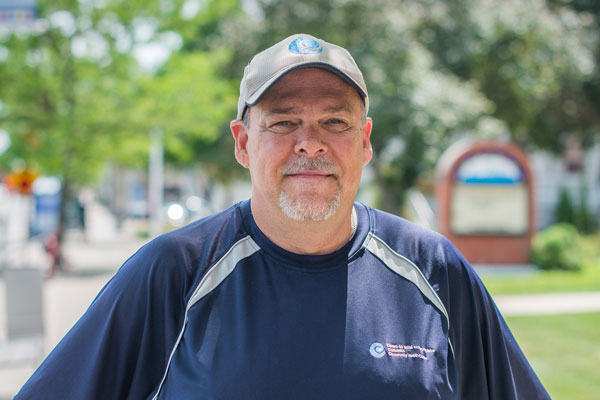 A man with a short grey beard and moustache in a dark blue shirt and ball-cap.