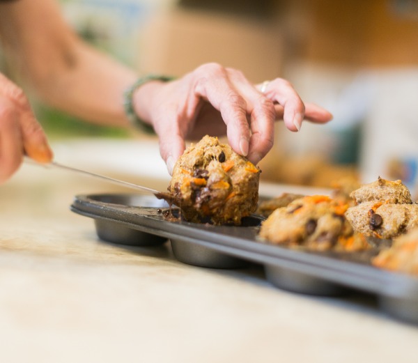 Hands removing freshly baked carrot muffins out of a pan.