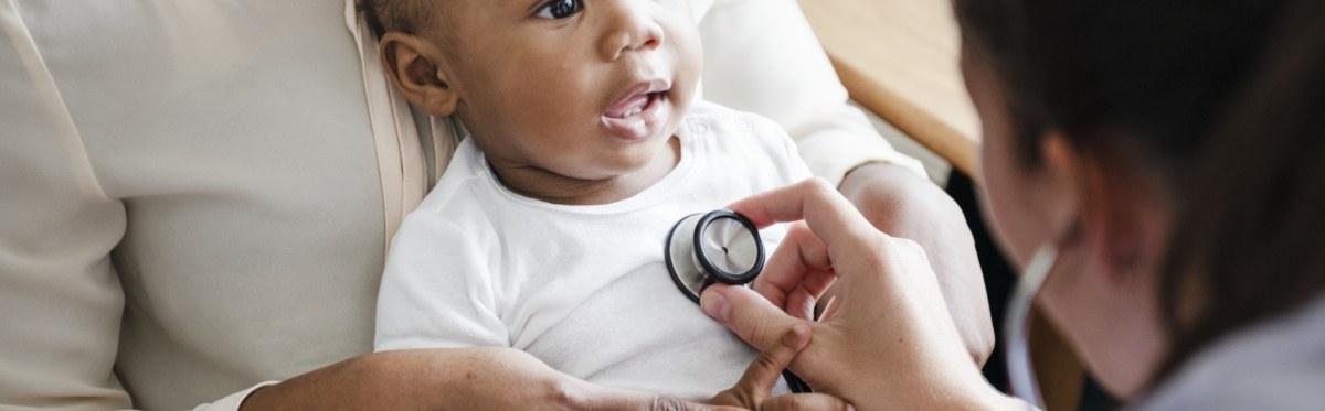 A female doctor holding a stethescope on the chest of a very small child.