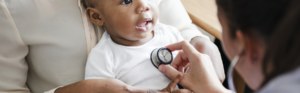 A female doctor holding a stethescope on the chest of a very small child.