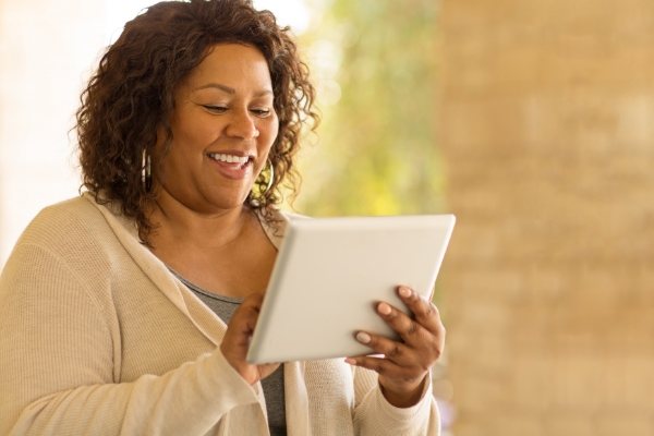 Smiling dark skinned woman with curly hair is smiling and tapping her tablet.