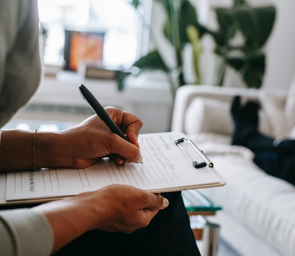 A person sits on a chair filling out a form on a clipboard.