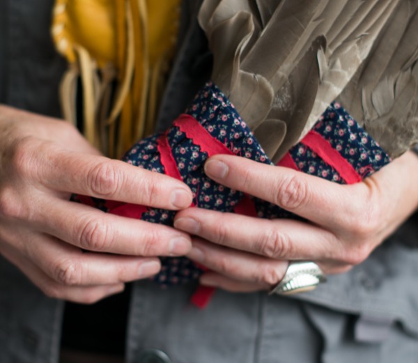 Hands hold two bundles of leaves wrapped in colourful fabric.