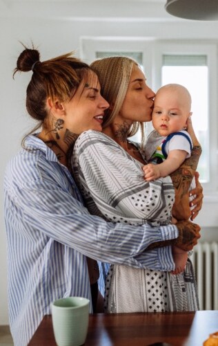 A woman hugging a baby and a second woman hugging both the woman and the baby.