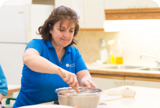 A woman stirring a metal bowl with a wooden spoon.